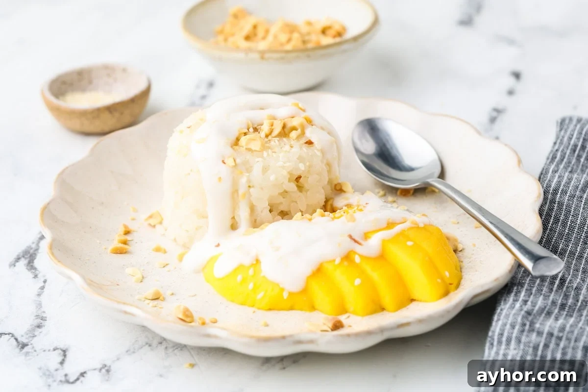 Mango Sticky Rice with Coconut Cream: Authentic Thai Dessert Recipe 13 Mango sticky rice plated with coconut cream and mango slices, served with a spoon on a light marble background.