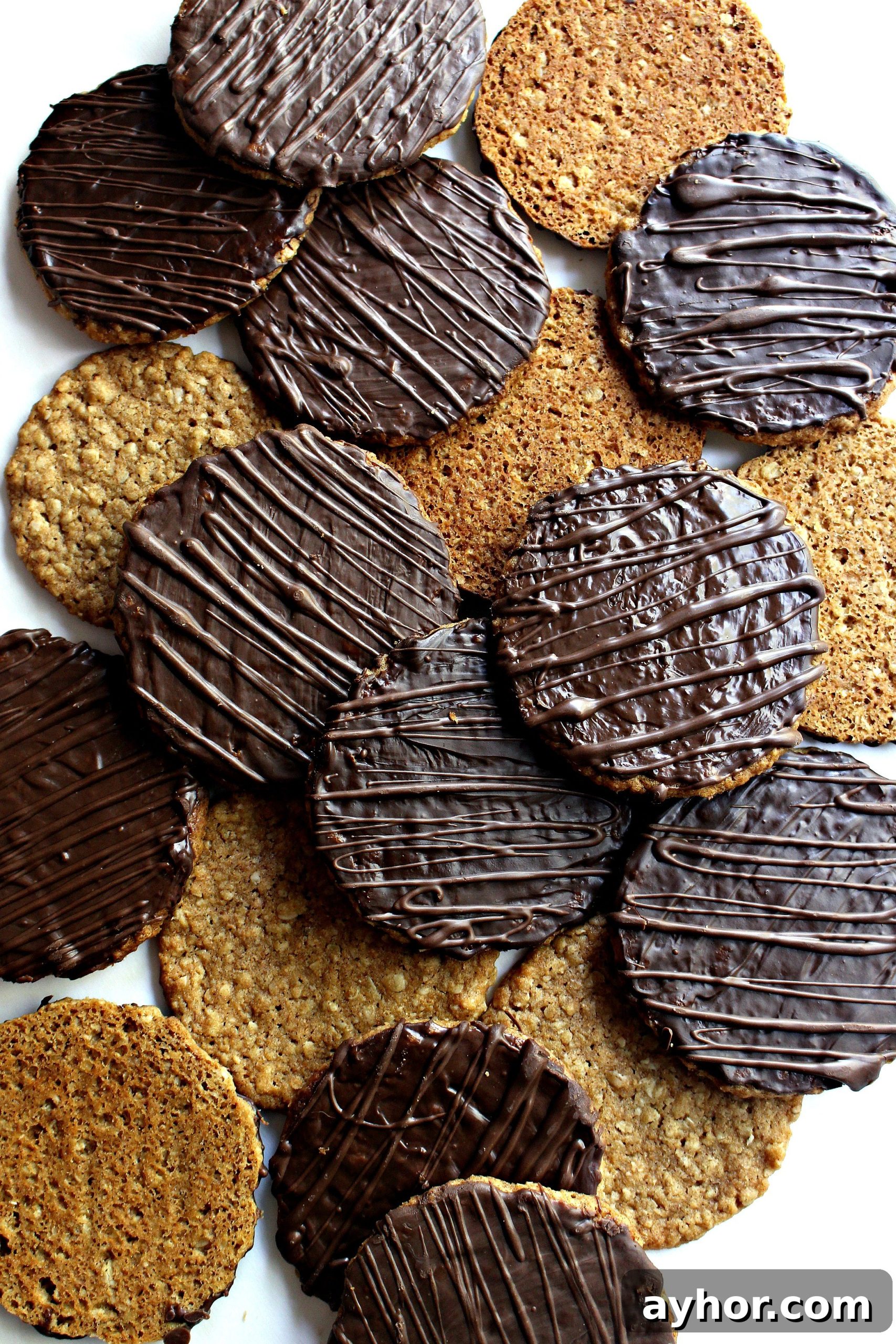 Chocolate-Covered Hobnob Oat Cookies Recipe 2 Hobnobs Oat Cookies scattered on a white surface, oat side or chocolate coated side facing up.