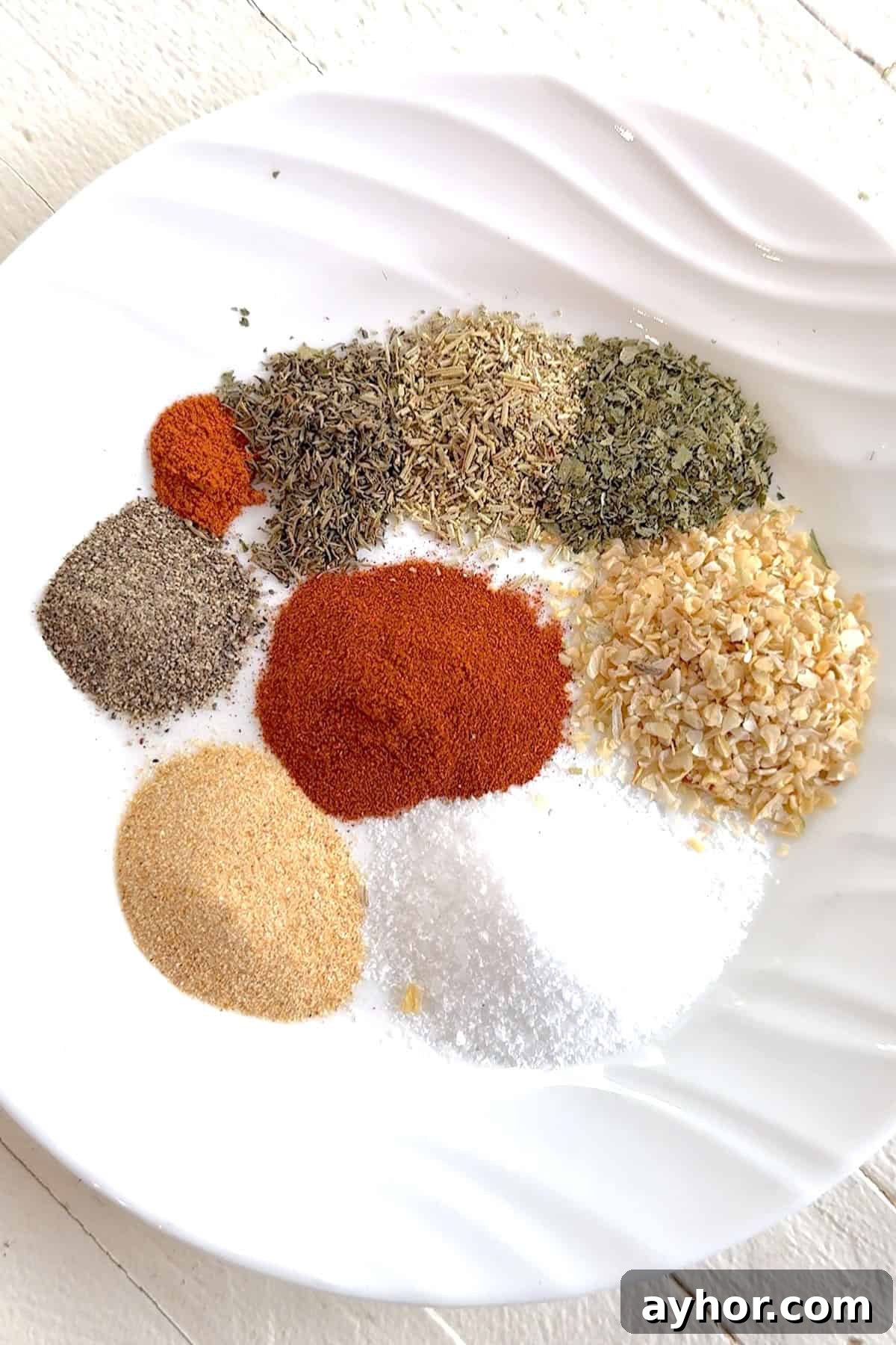 All the ingredients needed for making Montreal chicken seasoning on a white plate.