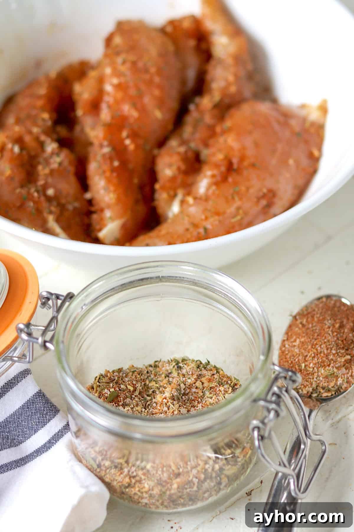 Montreal chicken seasoning in a jar and a bowl of raw chicken breast tenders covered in seasoning.