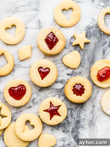Homemade jam-filled shortbread cookies with little cutout windows shaped like hearts and stars.