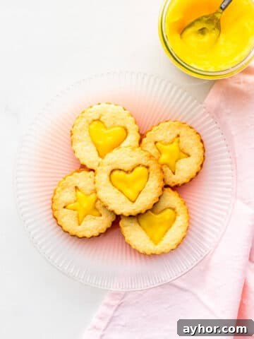 A plate of lemon curd-filled shortbread cookies with a jar of lemon curd on the side.