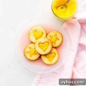 A plate of lemon curd-filled shortbread cookies with a jar of lemon curd on the side.