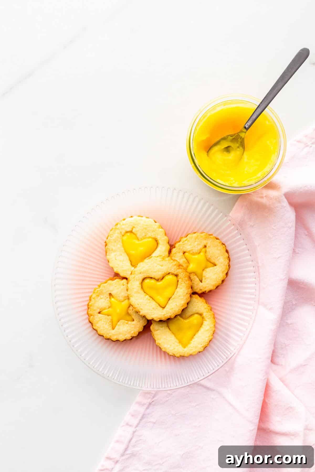 A plate of lemon-curd filled cookies with a jar of lemon curd on the side.