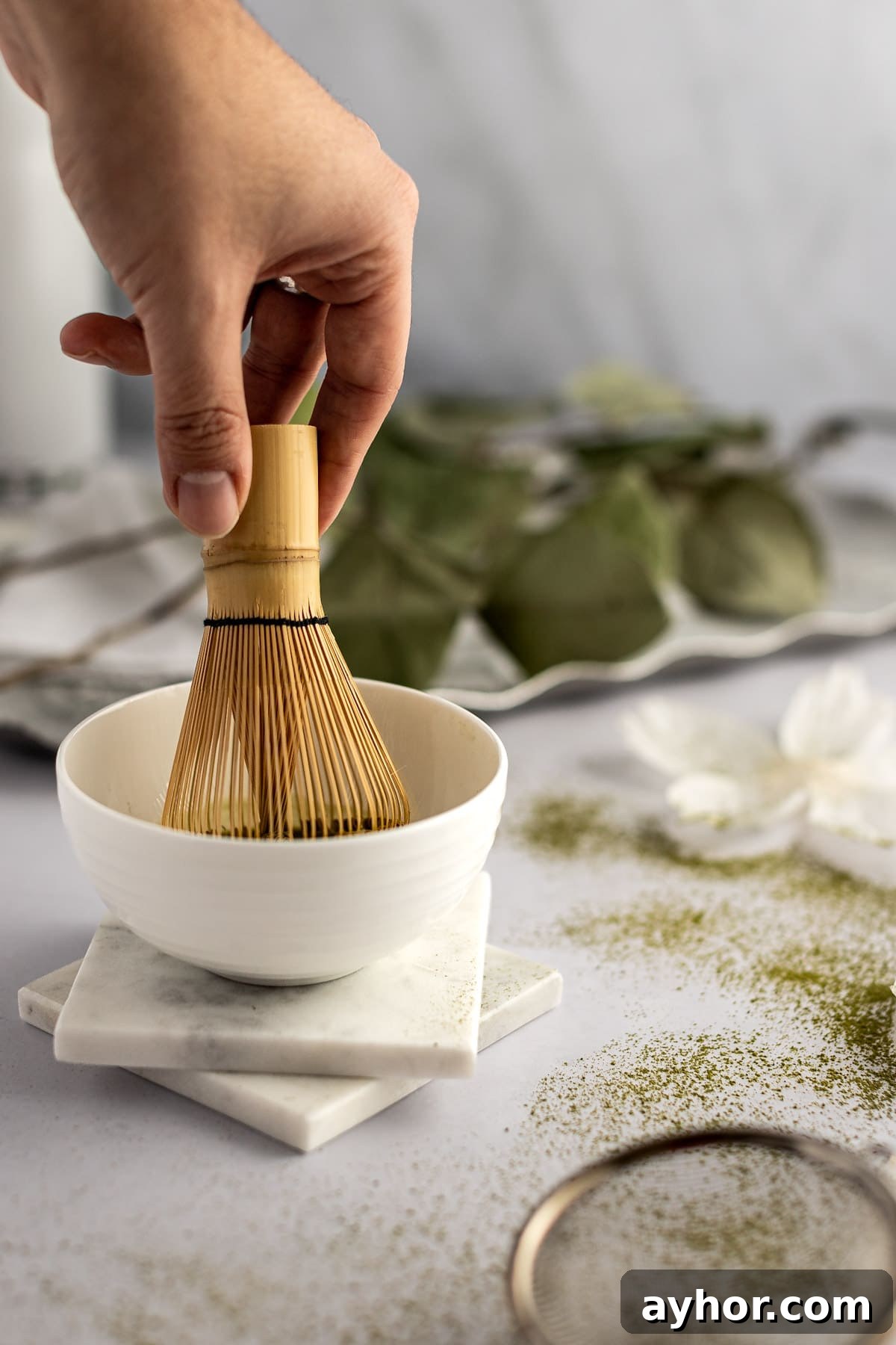 A holding a bamboo matcha whisk and stirring the matcha powder into the water to dissolve it.
