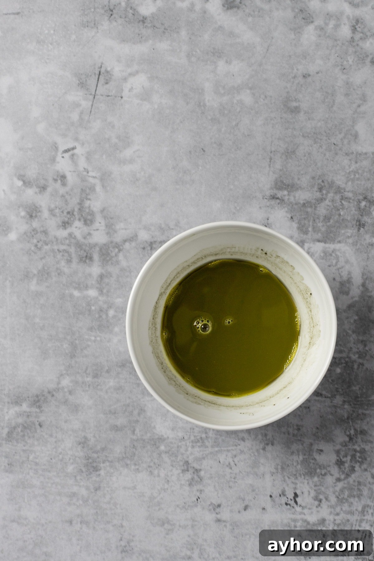 A small white bowl filled with matcha powder and water, after being mixed together with a whisk.