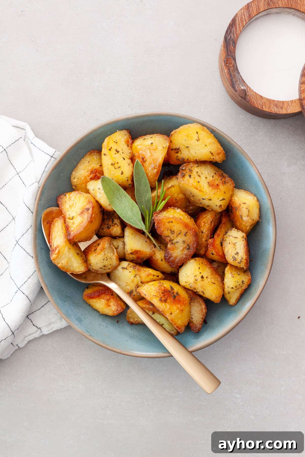A green serving bowl of crispy herb roasted potatoes with a gold spoon.