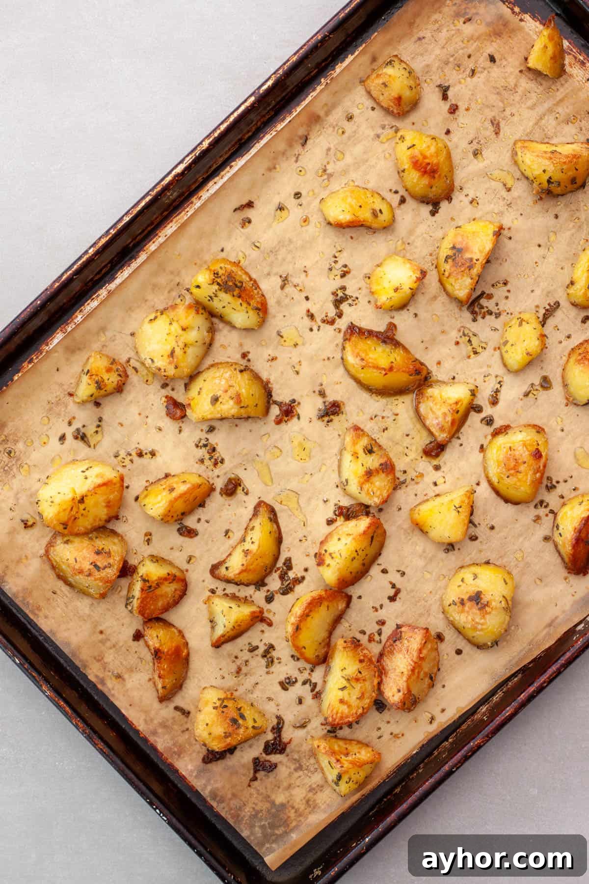 Freshly roasted herb potatoes on a parchment lined baking sheet.