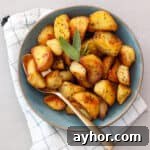 A green serving bowl of crispy herb roasted potatoes with a gold spoon.