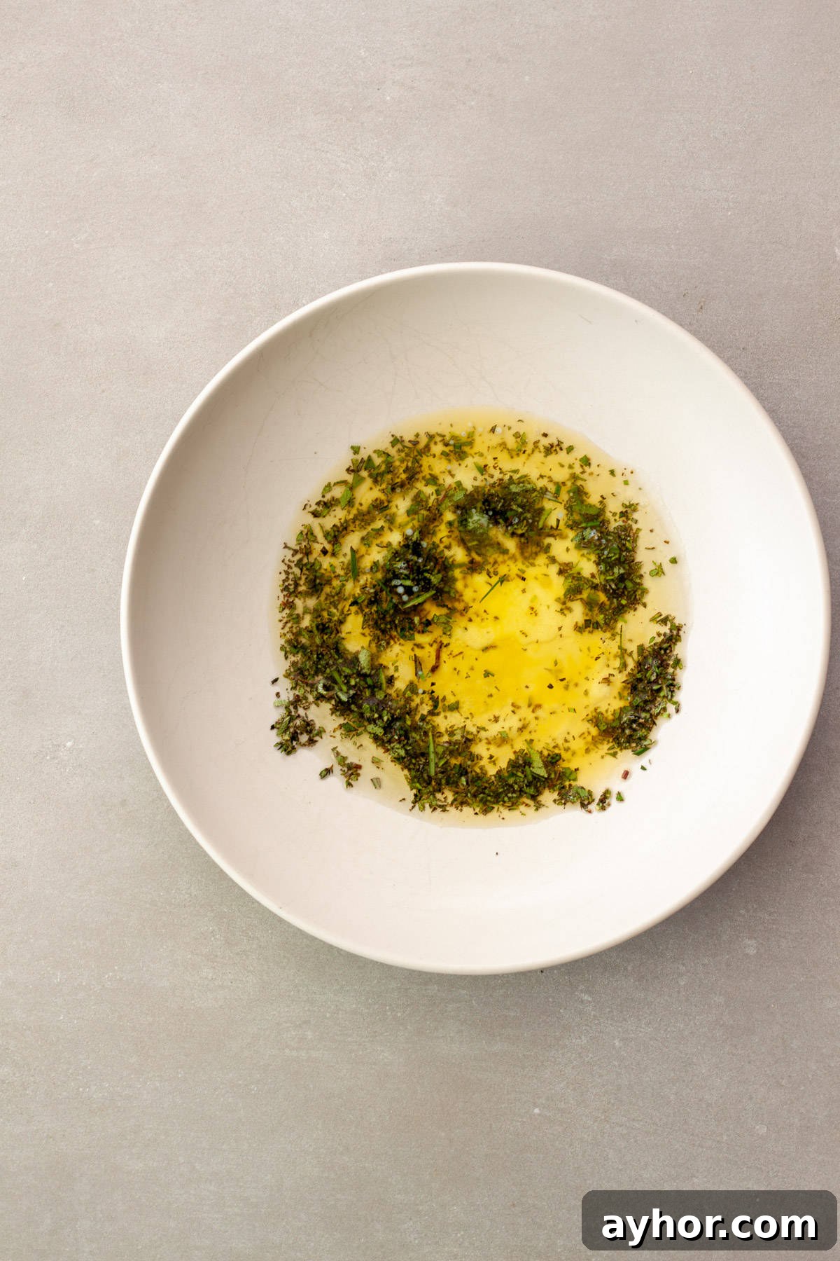 Melted butter, oil and fresh chopped herbs in a white mixing bowl.