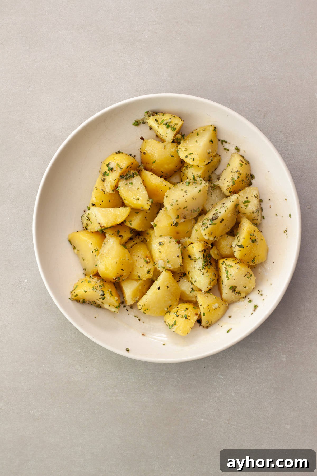Partially cooked potatoes in a bowl with butter, oil and fresh herbs.
