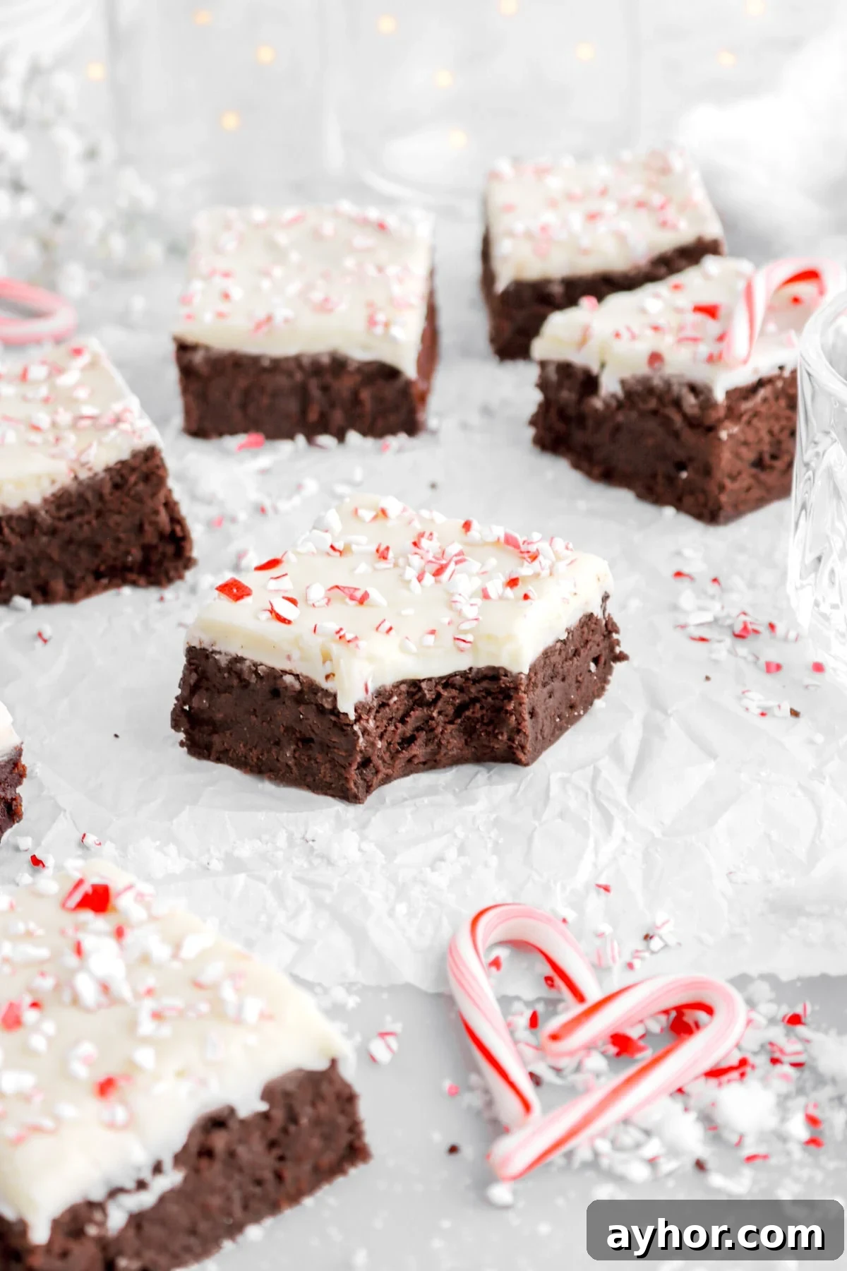 close up image of peppermint bark brownie with bite missing with more brownies around on parchment paper.