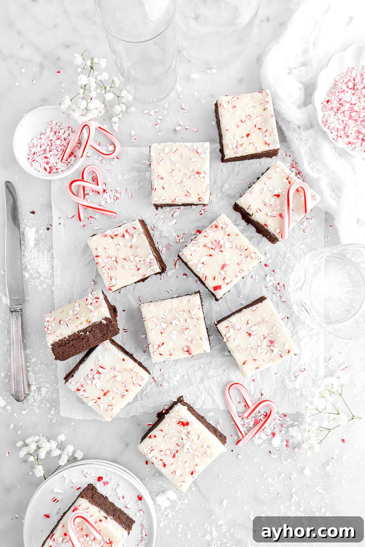 overhead image of peppermint bark brownies on parchment paper with mini candy canes and crushed peppermint around.