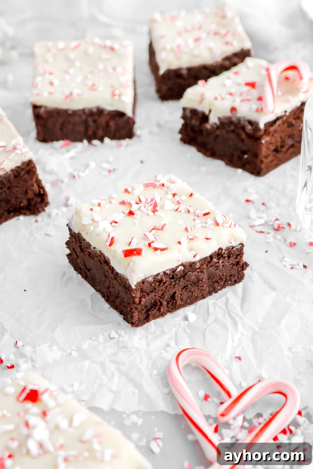 peppermint bark brownie on parchment paper with more brownies behind and mini candy canes around.