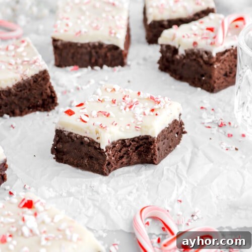 close up image of peppermint bark brownie with bite missing with more brownies around on parchment paper.