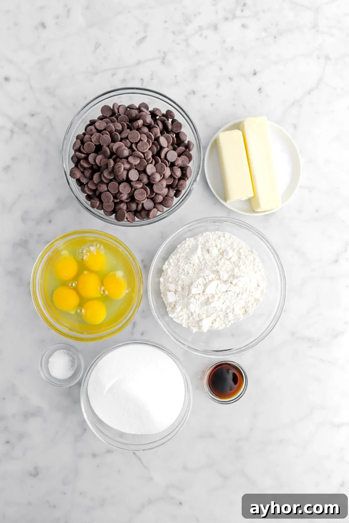 chocolate chips, butter, flour, eggs, salt, sugar, and vanilla on marble surface.