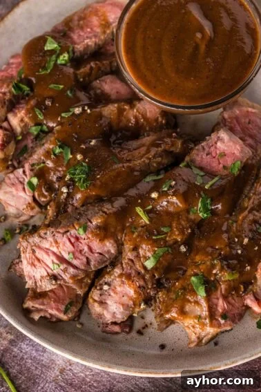 Sliced medium-rare steak topped with a1 sauce, garnished with chopped herbs, served on a plate with extra sauce in a small bowl.