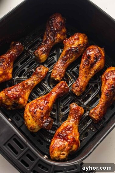 Eight glazed chicken drumsticks are arranged in a single layer inside the basket of an air fryer, cooked to a golden brown.