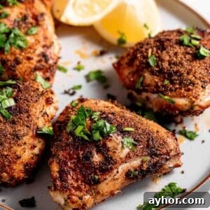 Chicken thighs on a white platter garnished with lemons and minced parsley.