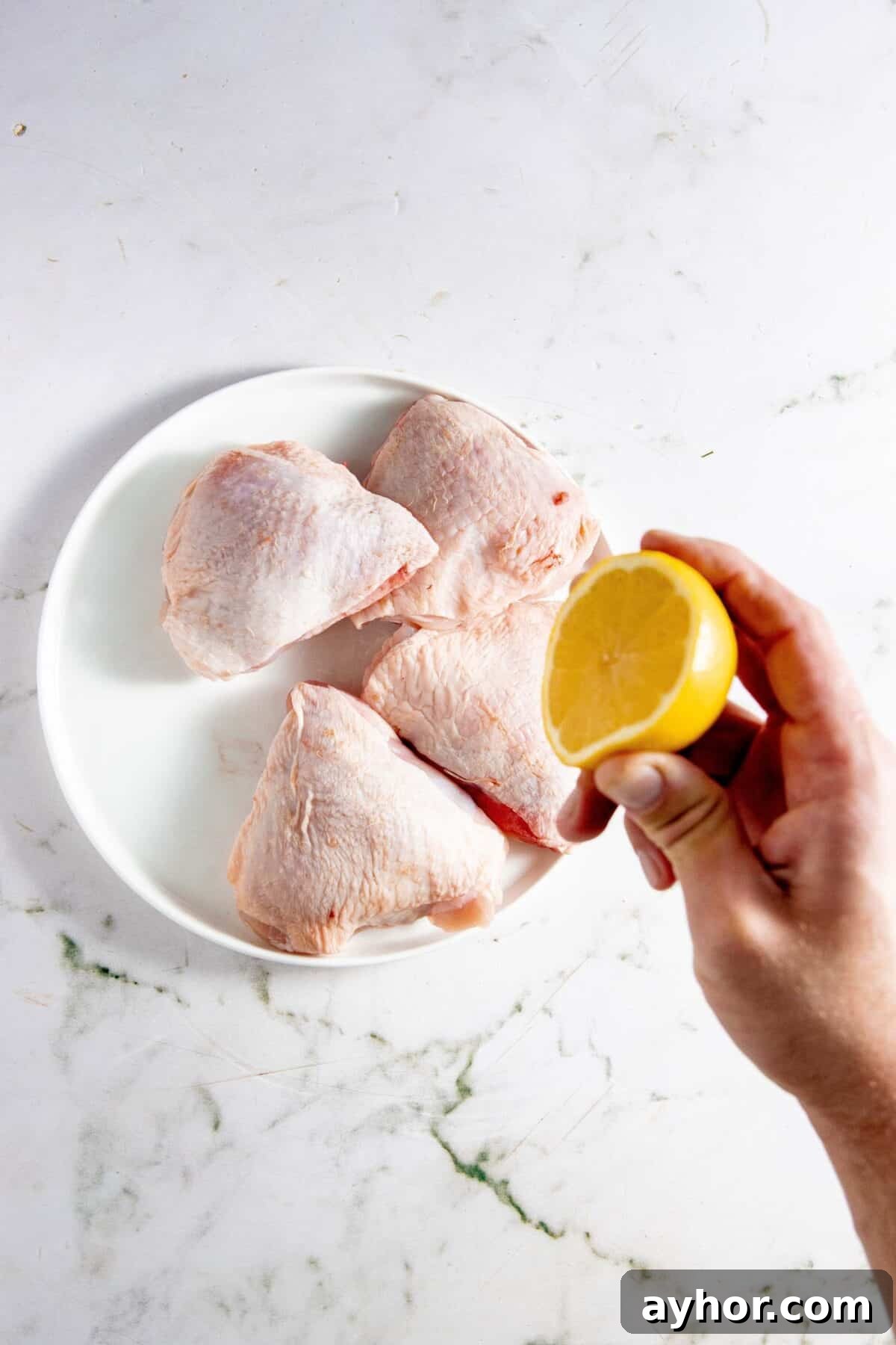 Hand squeezing lemon over chicken thighs.
