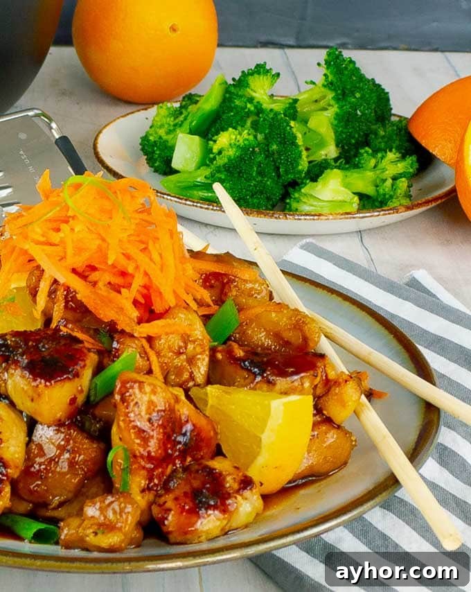 plate of sticky orange chicken with broccoli in the background