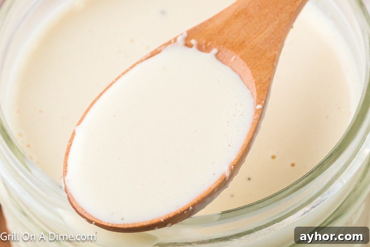 Alabama White BBQ Sauce Recipe: Tangy Homemade Chicken & Pork Glaze 2 White sauce in a jar with a serving on a wooden spoon