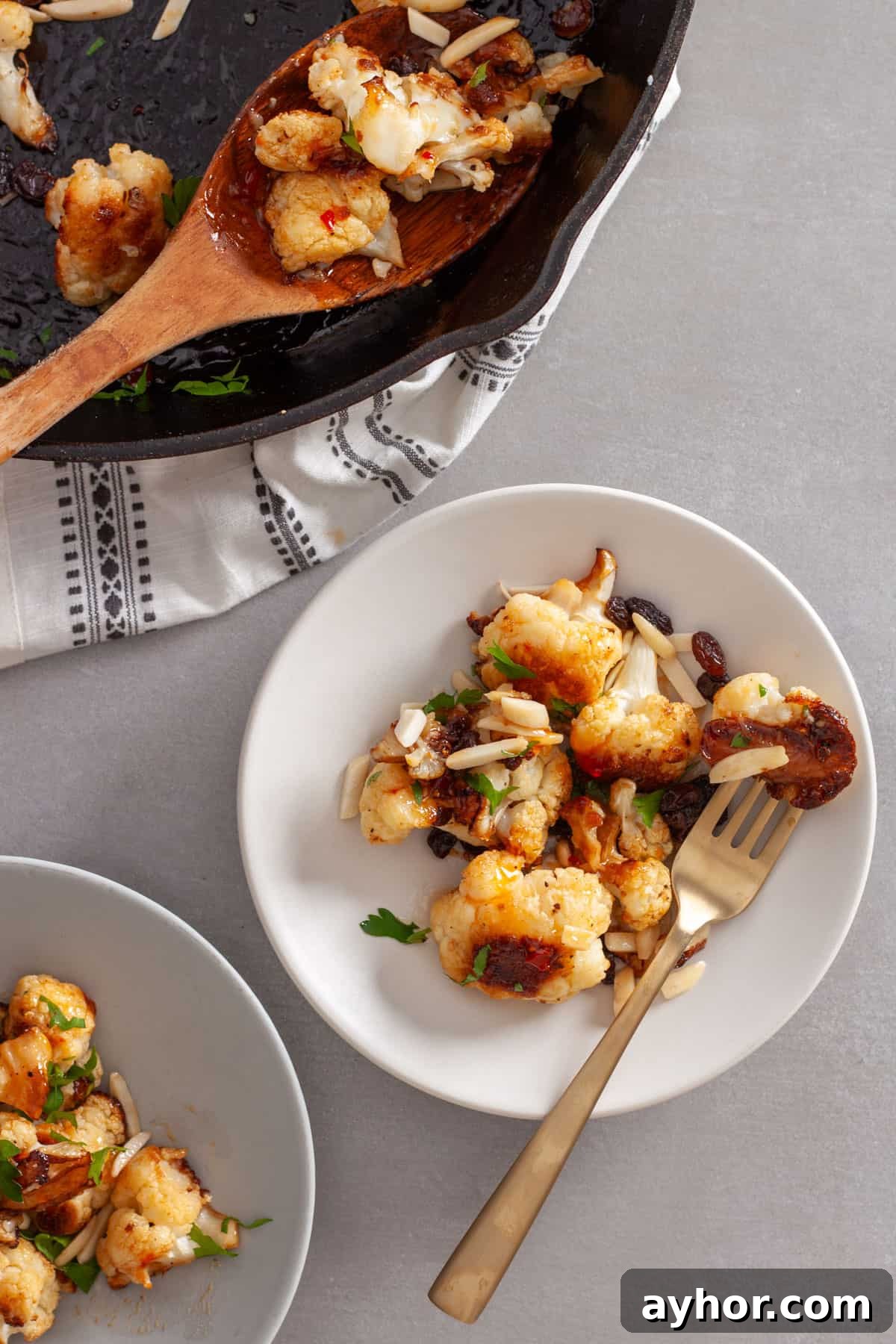 A serving of sweet chili roasted cauliflower on a white plate with a skillet to the side.
