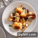 A serving of sweet chili roasted cauliflower on a white plate with a skillet to the side.