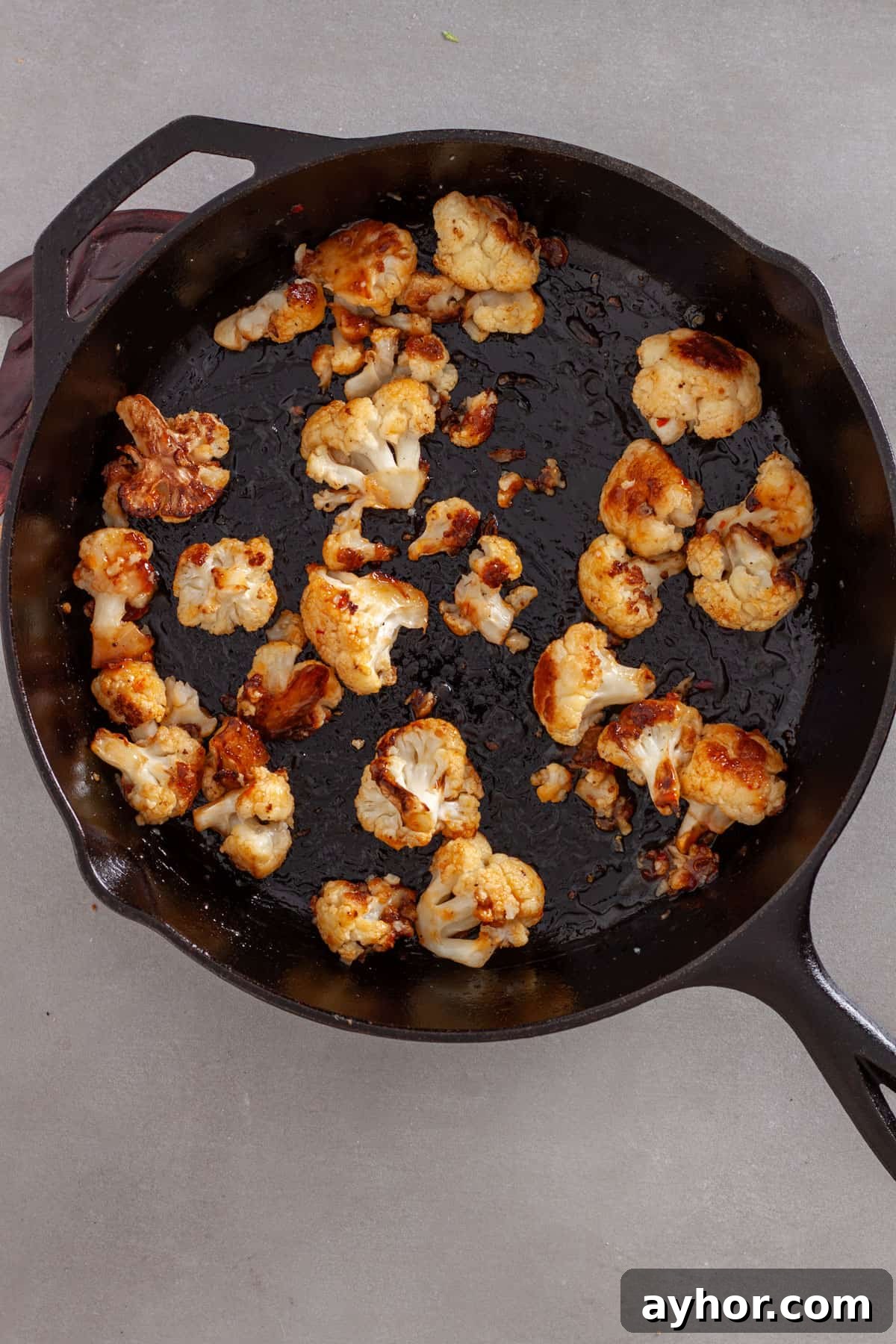 Seared cauliflower florets tossed with sweet chili sauce in a cast iron skillet.