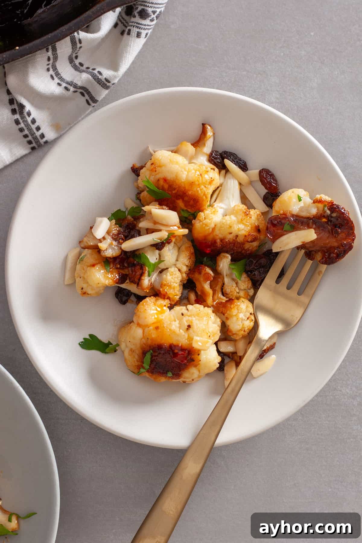 A small white plate with sweet chili roasted cauliflower and a fork piercing one cauliflower.