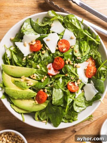 A serving bowl of spinach and arugula salad with a lemon thyme vinaigrette on a butcherblock countertop.
