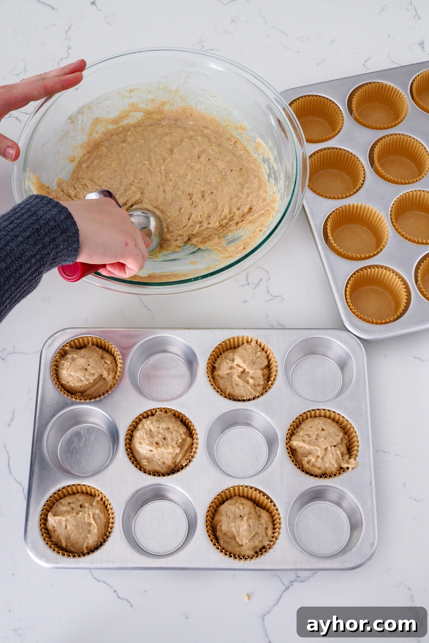 Caramel Chai Muffins Recipe — Warm Spiced Muffins with Caramel 7 A hand fills muffin cups with caramel chai muffin batter. The muffin pan has every other hole lined.