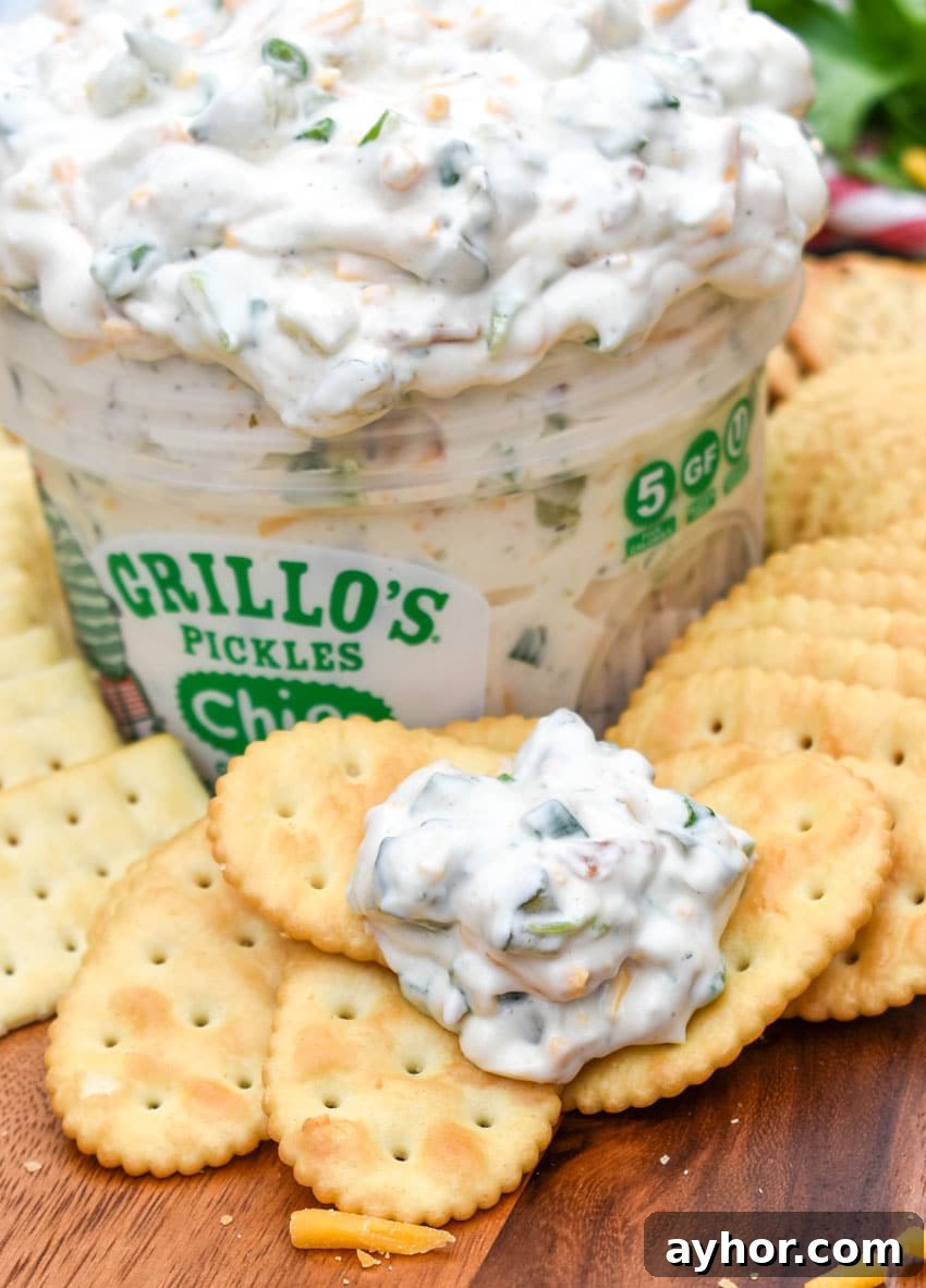 a cracker topped with creamy dill pickle dip resting on a wooden cutting board