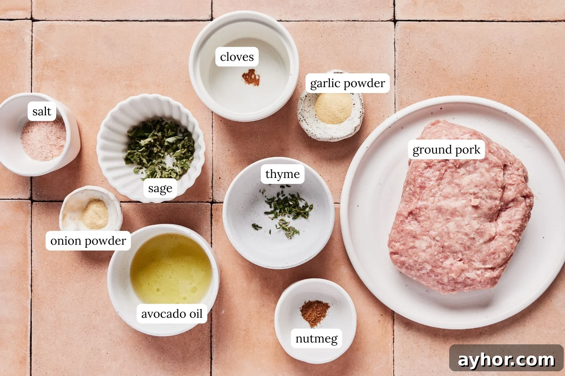 Ingredients for breakfast pork sausage laid out and labeled on a pink tiled countertop.