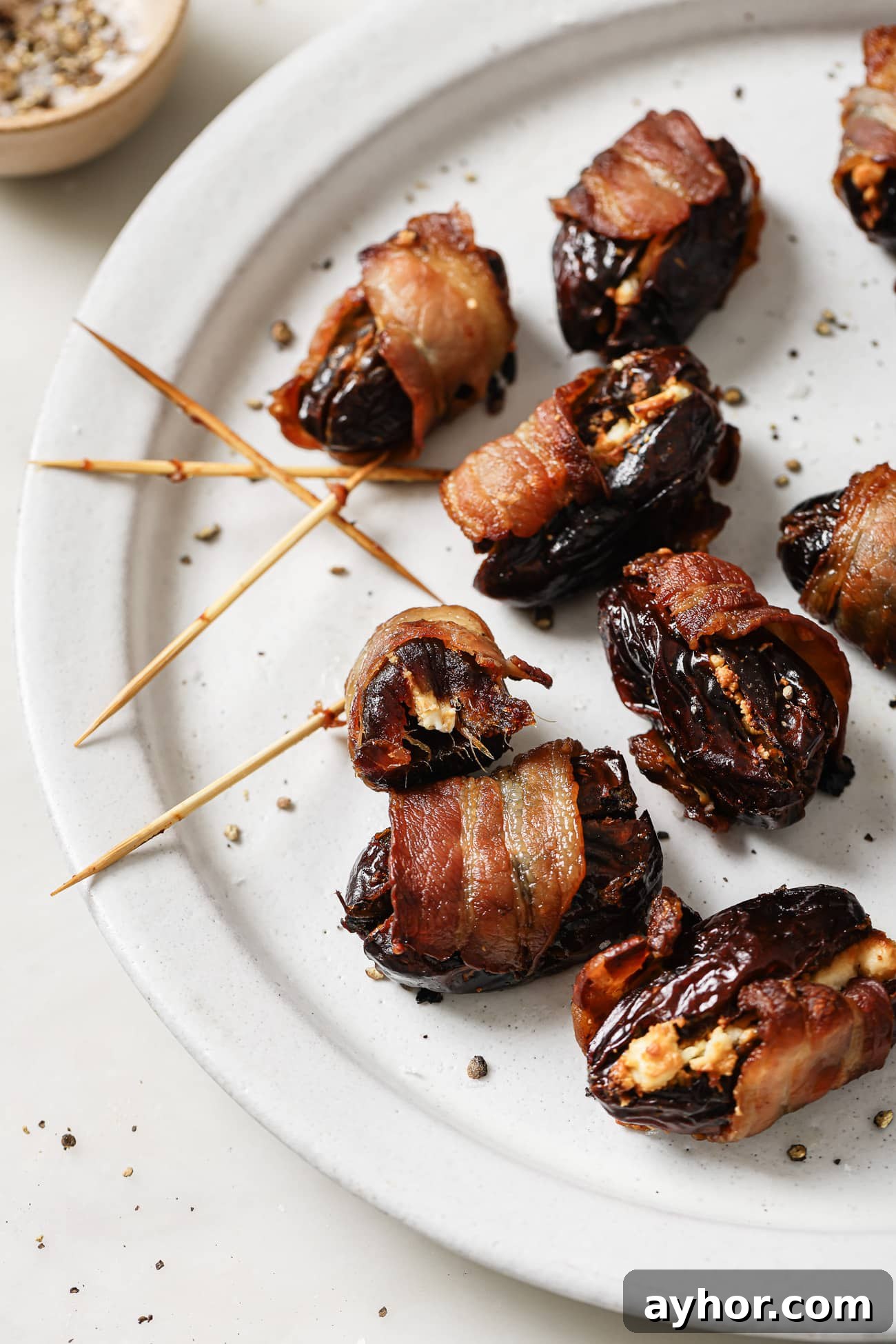 Bacon-Wrapped Dates: Sweet and Savory Appetizer Recipe 5 Close up of bacon-wrapped dates on a white plate.