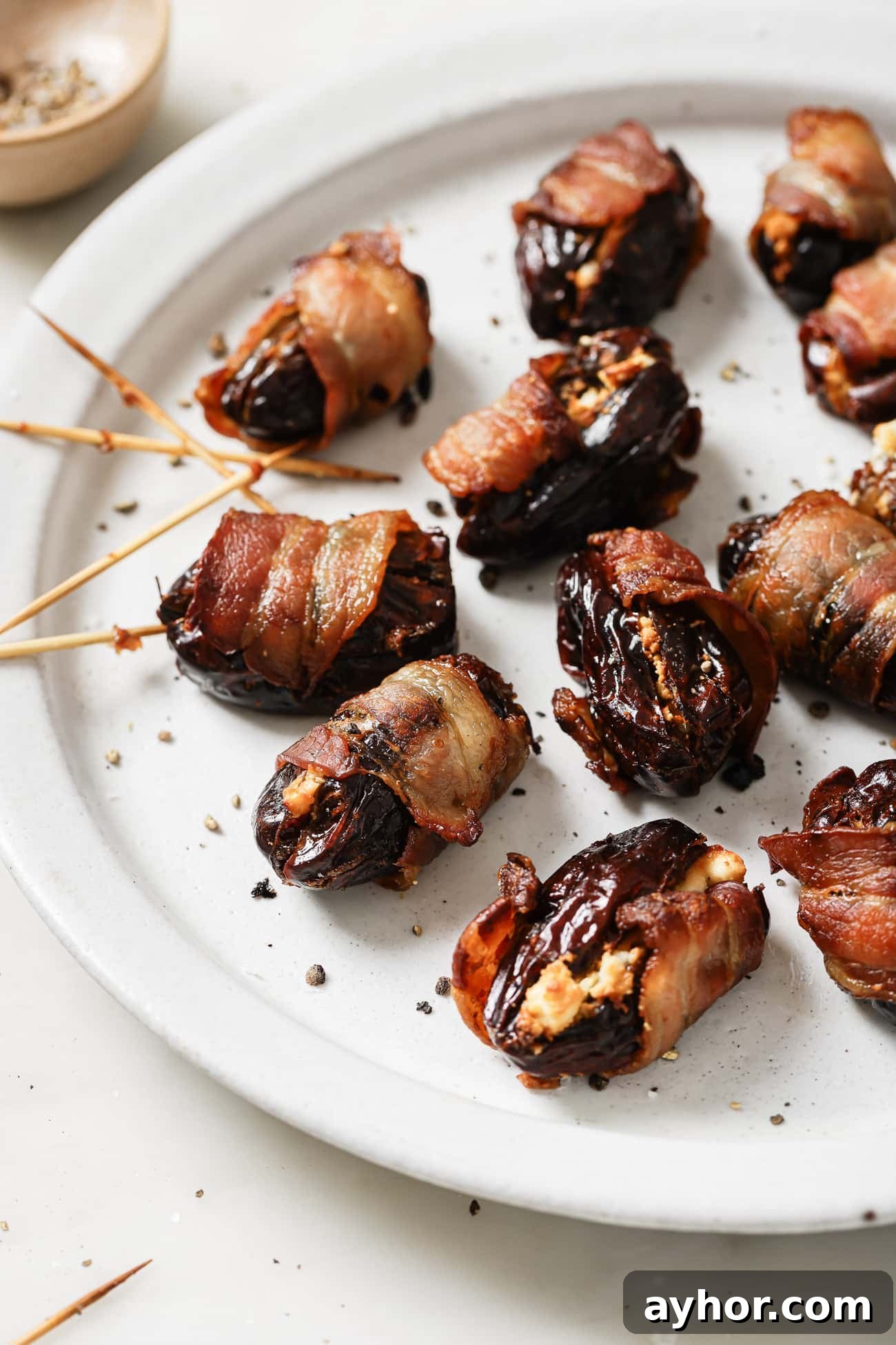 Bacon-Wrapped Dates: Sweet and Savory Appetizer Recipe 6 Close up of bacon-wrapped dates on a white plate.