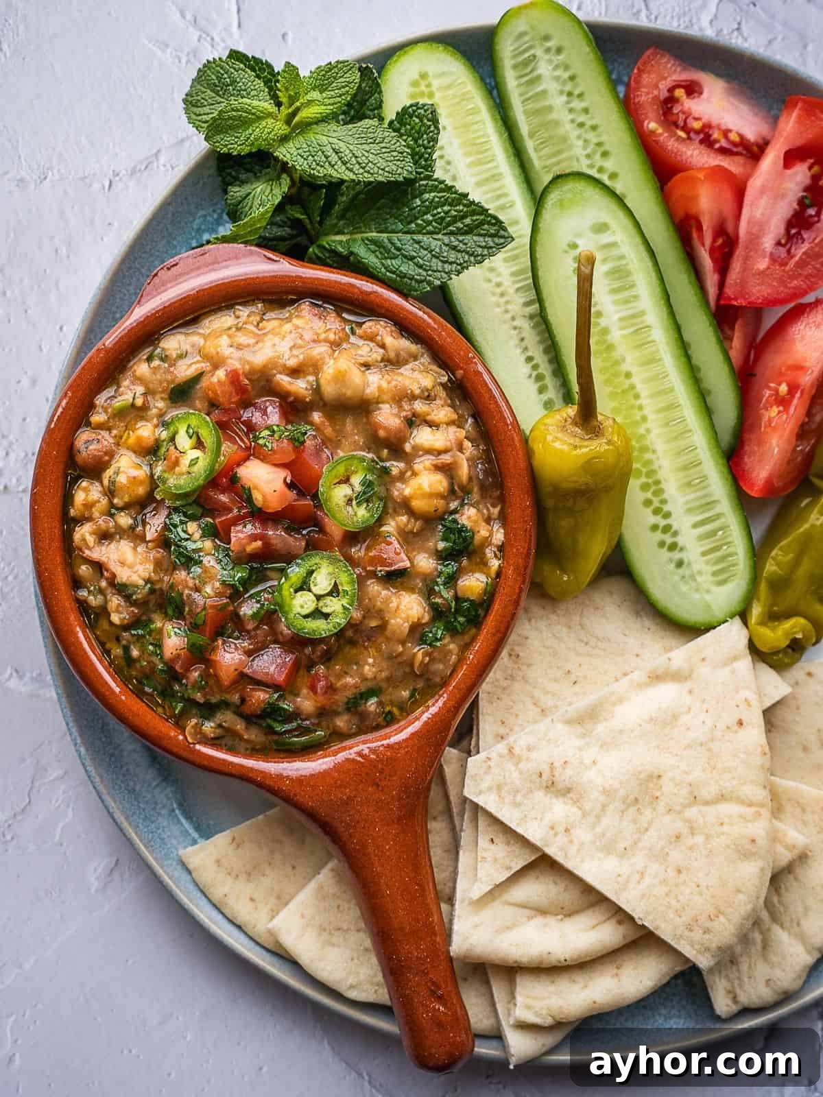 Levantine Ful Medames: Classic Chickpea & Fava Bean Stew Recipe 2 Platter with ful medames, sliced cucumbers, sliced tomatoes, and pita triangles.