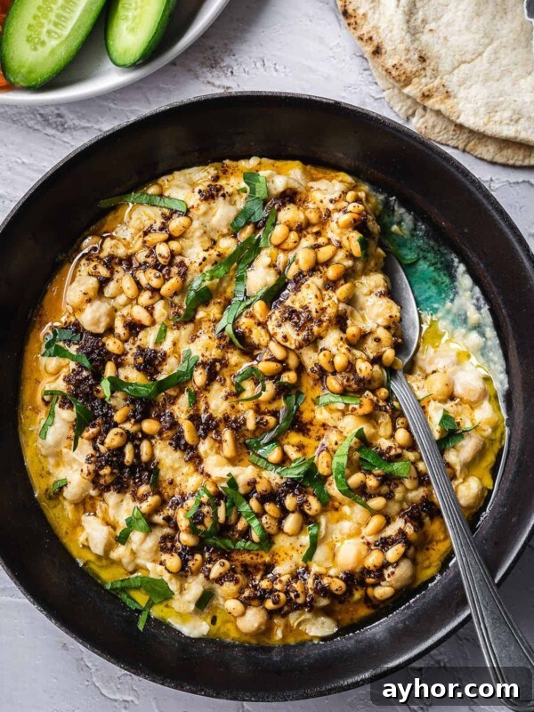 Levantine Ful Medames: Classic Chickpea & Fava Bean Stew Recipe 11 Bowl of warm chickpeas and tahini, garnished with parsley and pine nuts served with sliced cucumbers and pita.