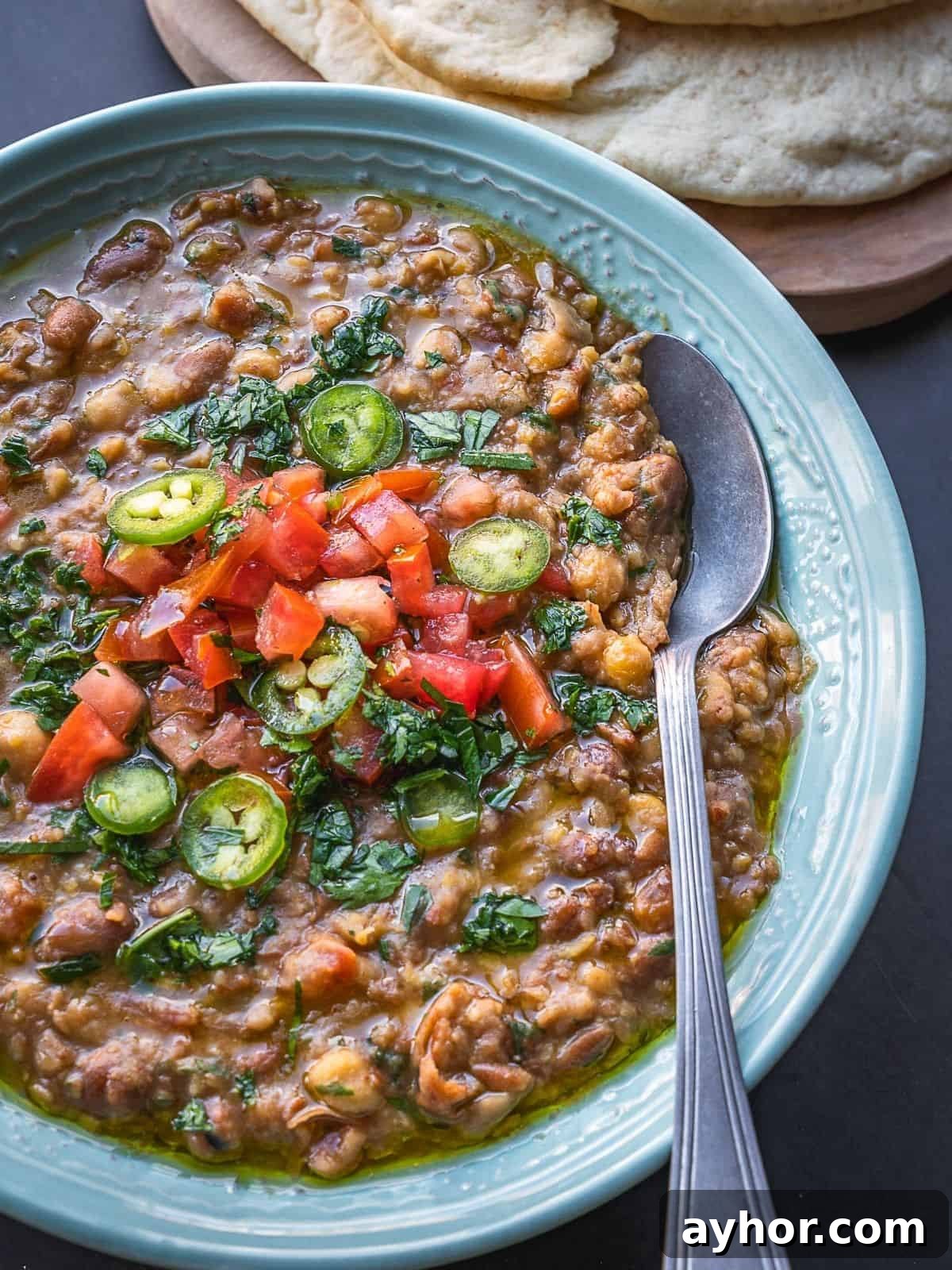 Levantine Ful Medames: Classic Chickpea & Fava Bean Stew Recipe 9 Bowl of mashed fava and chickpeas topped with diced tomatoes and parsley.