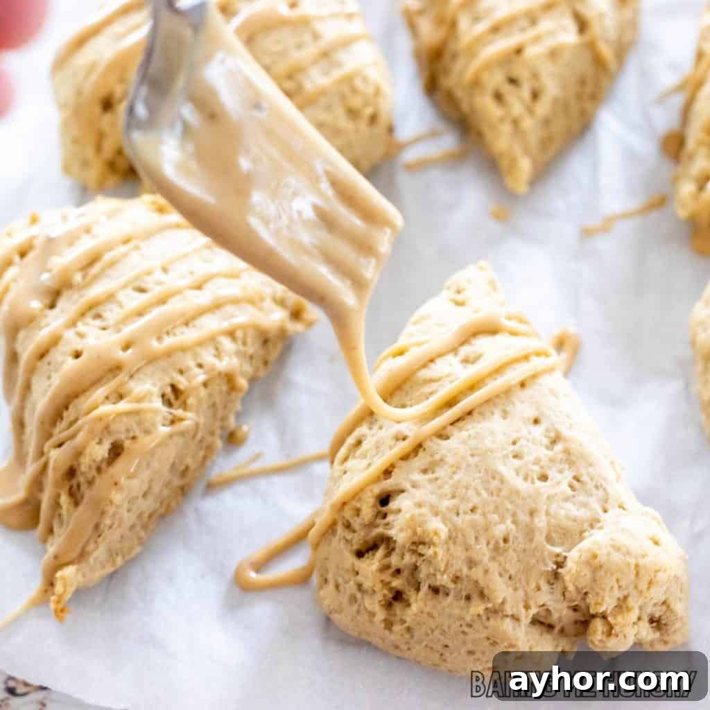 coffee scones on parchment being drizzled with glaze from a fork