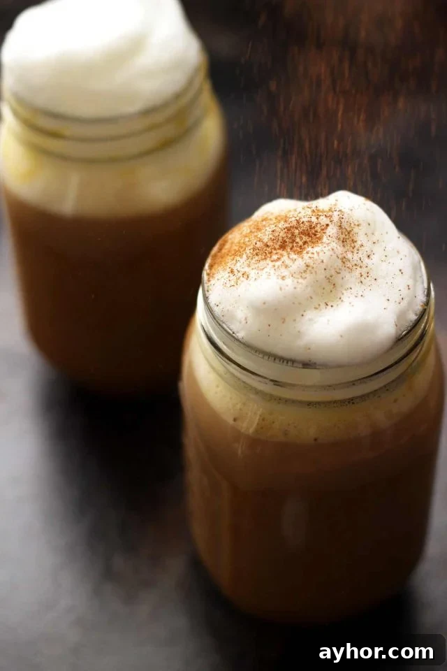 Healthy Vegan Pumpkin Spice Latte in a Mason Jar Topped with Cashew Whipped Milk Being Sprinkled with Cinnamon