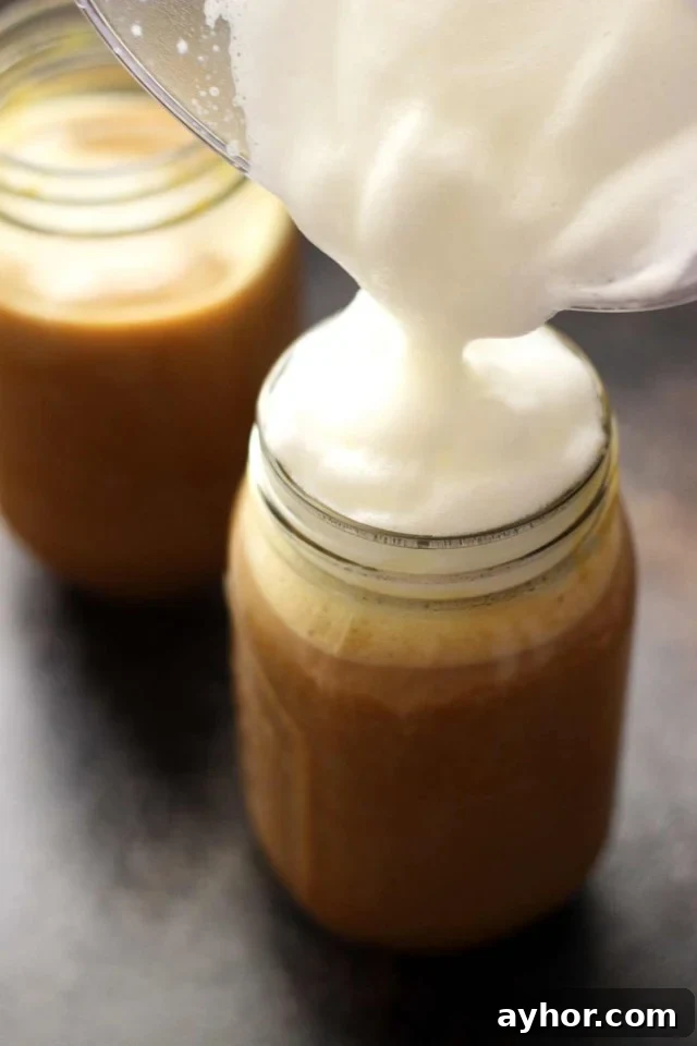 Healthy Vegan Pumpkin Spice Latte in a Mason Jar Topped with Cashew Whipped Milk Being Poured on Top