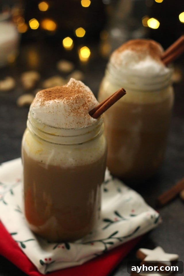 Healthy Vegan Pumpkin Spice Latte in a Mason Jar Topped with Cashew Whipped Milk in a Christmas Setup with Lights in the Background