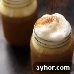 Healthy Vegan Pumpkin Spice Latte in a Mason Jar Topped with Cashew Whipped Milk Being Sprinkled with Cinnamon