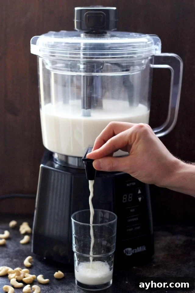 Healthy Vegan Pumpkin Spice Latte - the NutraMilk Dispensing Nut Milk in a Glass with Cashews Lying Around