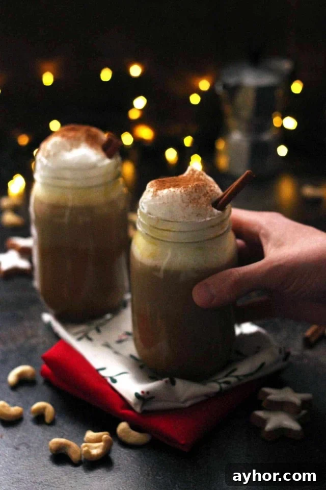 Hand Holding a Glass of Healthy Vegan Pumpkin Spice Latte with Lights and Another Jar in the Background