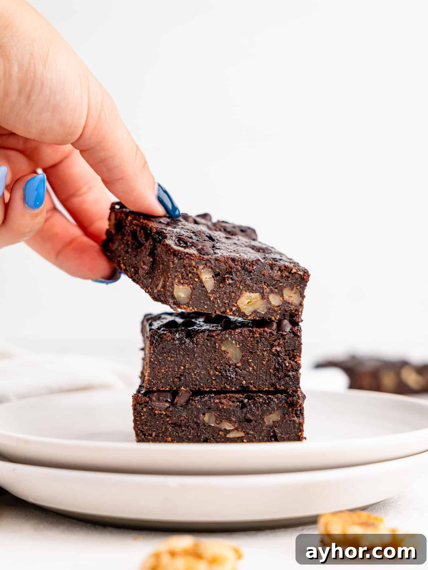 Three healthy brownies on a white plate, a hand is holding the top brownie.