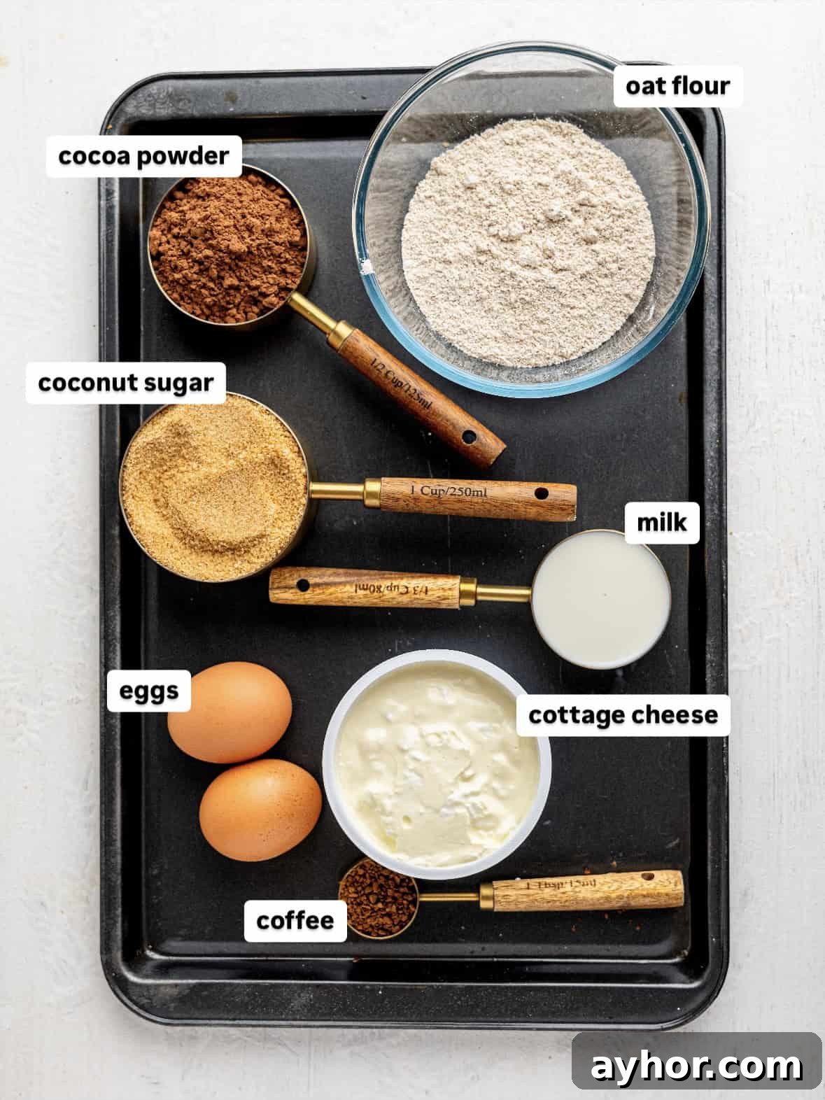 Ingredients for cottage cheese brownies in measuring cups on a baking tray.
