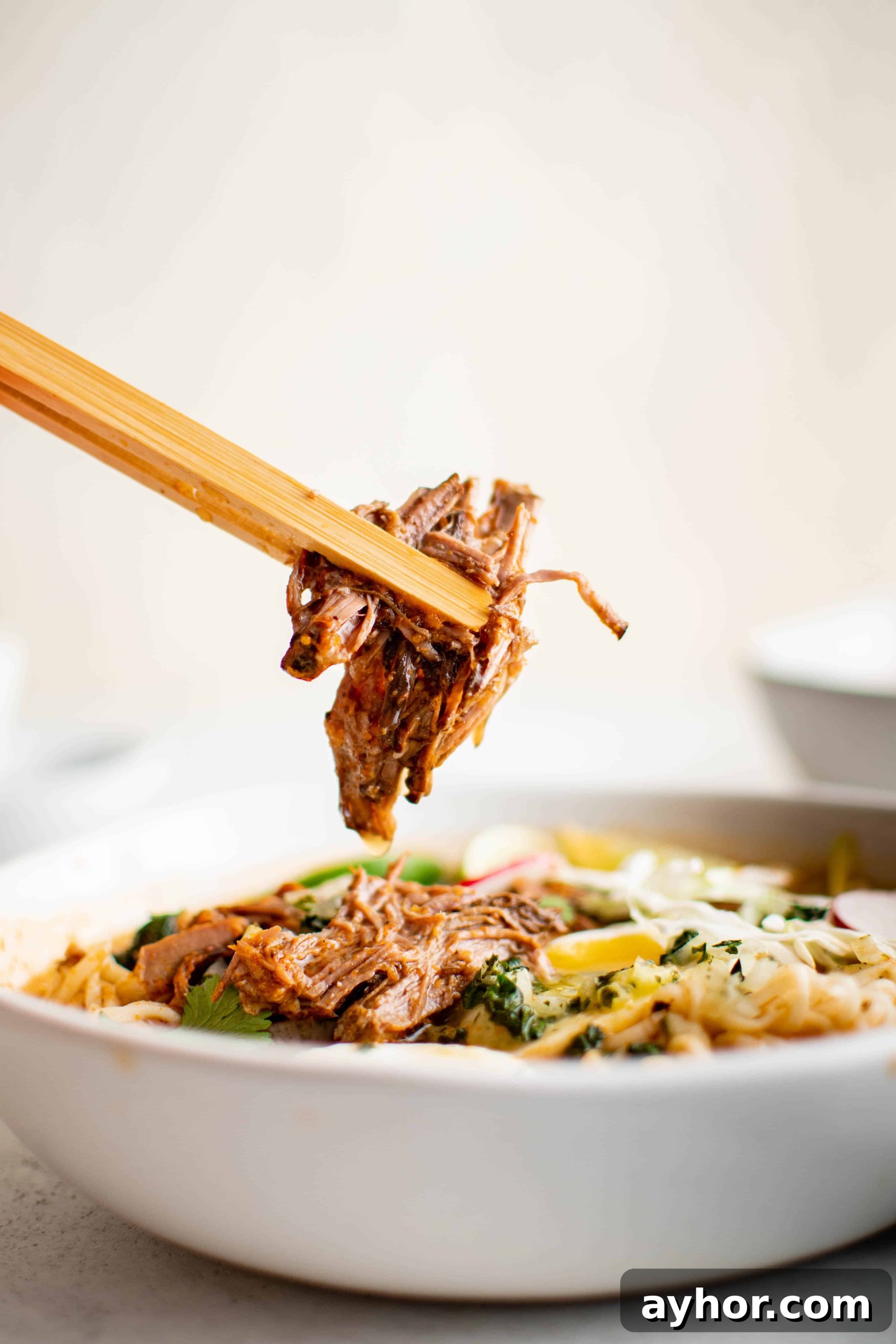 Birria Ramen Recipe: Flavorful Mexican-Style Beef Ramen 3 Chopsticks picking out shredded birria beef from a large bowl of birria ramen.