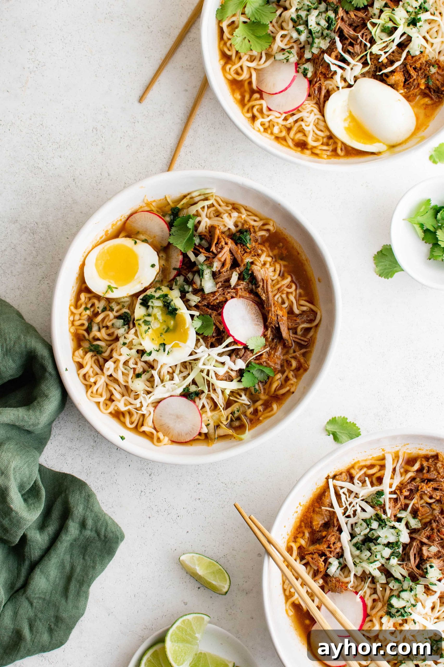 Birria Ramen Recipe: Flavorful Mexican-Style Beef Ramen 7 Three white bowls filled with ramen noodles, shredded beef, soft boiled eggs, and garnishes in a rich birria broth.